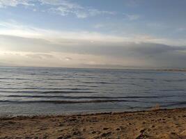 Tranquil shoreline at dusk with gentle waves lapping against the sandy beach under a vast, colorful sky photo