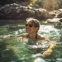Smiling woman swimming in clear water on a sunny day, wearing sunglasses and enjoying nature in a serene environment photo