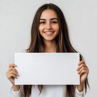 Smiling young woman holding blank white sign in front of her for advertisement or message in a minimalist background photo