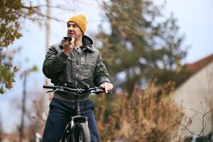 Man Using Cell Phone while Standing Next to Bike photo