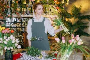 A woman in her florist shop collects bouquets of flowers. The concept of a small business. Bouquets of tulips for the holiday on March 8. photo