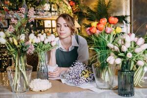 A woman in her florist shop collects bouquets of flowers. The concept of a small business. Bouquets of tulips for the holiday on March 8. photo