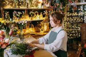 A woman in her florist shop collects bouquets of flowers. The concept of a small business. Bouquets of tulips for the holiday on March 8. photo