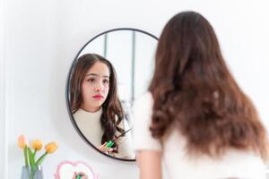 Teenage girl applying makeup, Teenage with freckle face applying makeup in front of a mirror at home photo