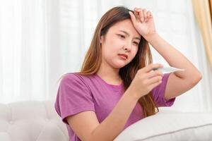 Asian woman having high fever while checking body temperature with digital thermometer photo