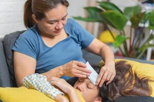 Mother using cold compress to taking care for sick daughter ill with high temperature on sofa at home photo