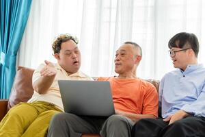 Senior asian man having a good time sitting on couch at home with adult son, Cheerful grandfather and grandson using laptop doing a call in living room photo
