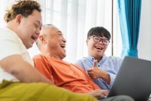 Cheerful grandfather and grandson using laptop doing a call in living room, Senior asian man having a good time sitting on couch at home with adult son photo