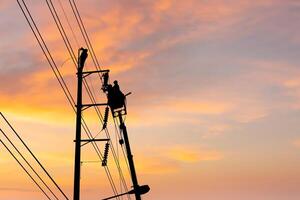 Silhouette of Electrician officer climbs a pole and uses a cable car to maintain a high voltage line system, Shadow of Electrician lineman repairman worker at climbing work on electric post power pole photo