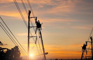 Silhouette of Electrician officer climbs a pole and uses a cable car to maintain a high voltage line system, Shadow of Electrician lineman repairman worker at climbing work on electric post power pole photo