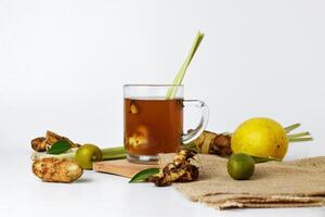 Hot red ginger drink in a glass cup with some raw ginger and lemon photo