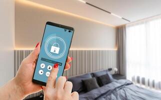 Young woman holding smart phone with launched security application at home. Concept of controlling and managing home security from a mobile device photo