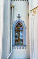 A series of pointed arched Gothic windows framed in gold with intricate lattice patterns adorn the exterior of a historic building. Captured in natural daylight, the windows reflect the surrounding photo
