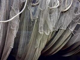 A detailed view of tangled fishing nets hanging from ropes, creating intricate layers of texture. The weathered appearance evokes the rugged life of fishermen and the maritime industry photo