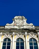The facade of an abandoned Baroque estate in Peterhof, Russia, with its once-glorious architecture now showing signs of decay. A wide-angle shot reveals intricate, weathered details under a bright photo