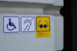 Signs indicating access for people with disabilities. Symbol of deaf and blind person next to wheelchair sign on wall of building entrance photo