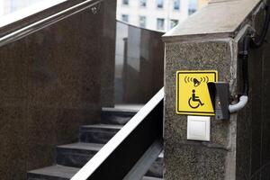 Wheelchair ramp with call button near stairs, yellow sign to indicate folding ramp for easy descent for persons with disabilities, accessible button and ramp equipment for the disabled on street photo