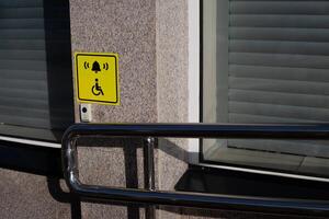 Hand rails to assist person in wheelchair next to handicap sign on wall and call button to assist person with disability, modern entrance to building with convenient ramp for people with disabilities photo