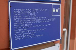 Sign with information in braille text for blind people in front of the building entrance. Accessible environment for people with disabilities, communication in language for people with low vision photo