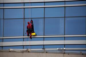 Heavy work with belay on ropes, climber rappels down the facade of building to wash windows, cleaning the facade of glass skyscraper photo