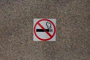 Sticker with crossed out cigarette on marble wall of building, ban on smoking in public place with special sign, social problem and smoking addiction photo