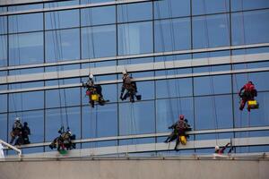 Group of climbers clean glass of skyscraper on special mounts with insurance, hard work at height, cleaning the exterior of glass office building photo