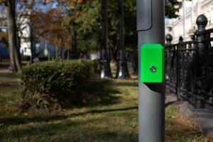 Control panel with button for pedestrians on pole, activate green traffic light signal for crossing the road along street in modern city against the backdrop of park photo