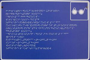 Blue sign with white dots of braille text. Braille alphabet to help people with blindness. Information for people with disabilities in frame with glasses sign photo