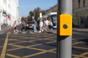 Button for changing traffic light signal for pedestrians to cross an intersection. Control panel for waiting to cross the road hangs on pole on the background of people cross road photo