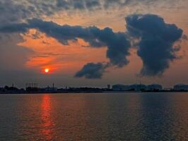 A sunset over the water with clouds and a large building photo