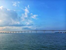 A boat is sailing across the ocean with a bridge in the background photo