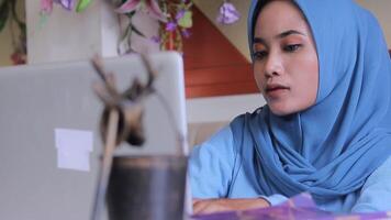 closeup of beautiful asian woman wearing a headscarf busy working on a task from the company typing in front of a laptop on a table in a coffee shop. for communication content, lifestyle, business video