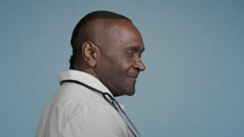 African american man doctor male professional physician medical worker healthcare therapist surgeon employee standing with back turning around looking camera smiling posing in studio blue background video