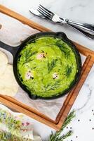 broccoli cream soup with herbs, cheese and tortillas in a frying pan, top view photo