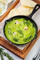 broccoli cream soup with herbs, cheese and tortillas in a frying pan, top view photo