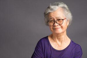 An elderly Asian woman looking at the camera with a smile while standing over a gray background photo