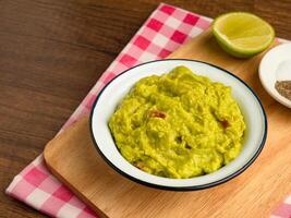 Fresh guacamole in a bowl on a wooden cutting board photo