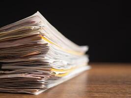 Stack of documents with binder clips on a wooden table with a black background photo