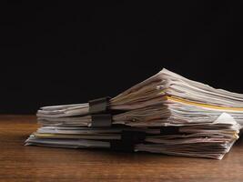 Stack of documents with binder clips on a wooden table with a black background photo
