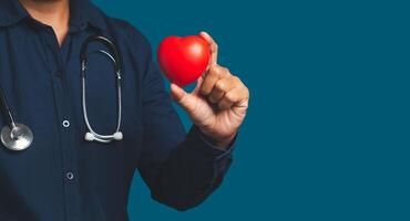 Hand of a doctor holding a red heart shape while standing on a blue background. photo