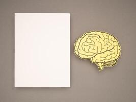Blank white paper and a brain shape made from yellow paper on a gray background photo