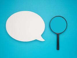 Top view of a blank speech bubble and a magnifying glass on a blue background photo