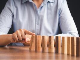 Risk and strategy in business concept. Close-up of hand push a wooden block on a line of domino photo