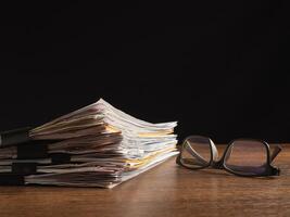 Stack of documents with binder clips and eyeglasses on a wooden table photo