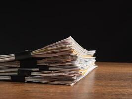 Stack of documents with binder clips on a wooden table with a black background photo