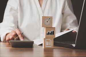 Woman using a calculator and three wooden cubes with icons business on the table in the office photo
