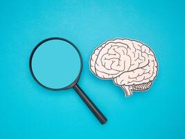 A brain shape made from paper and a magnifying glass on a blue background photo
