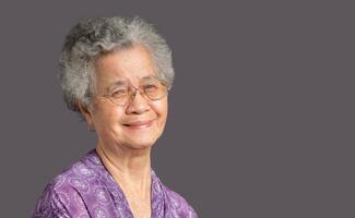 Cheerful an elderly Asian woman with short gray hair looking at the camera with a smile while standing on gray background in the studio. photo