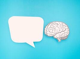 White speech bubble and a brain shape made from paper on a blue background photo