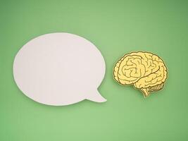 White speech bubble and a brain shape made from paper on a green background photo